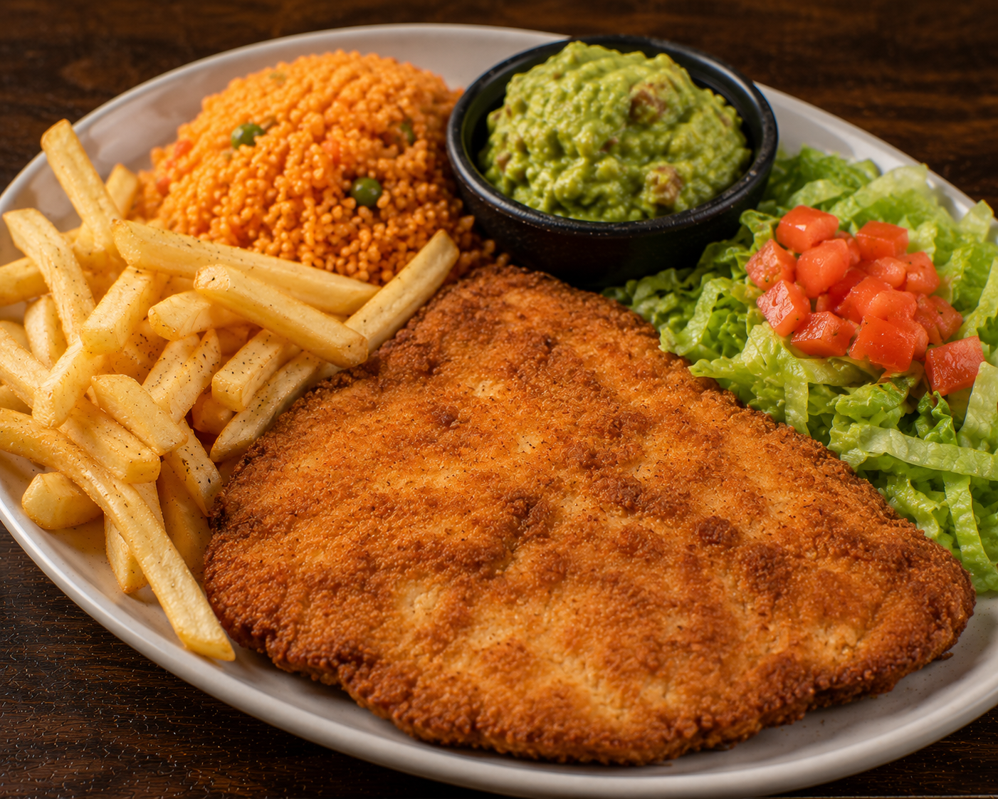 Chicken Breaded plate served with fries, rice, guacamole, lettuce, and tomato on a white plate