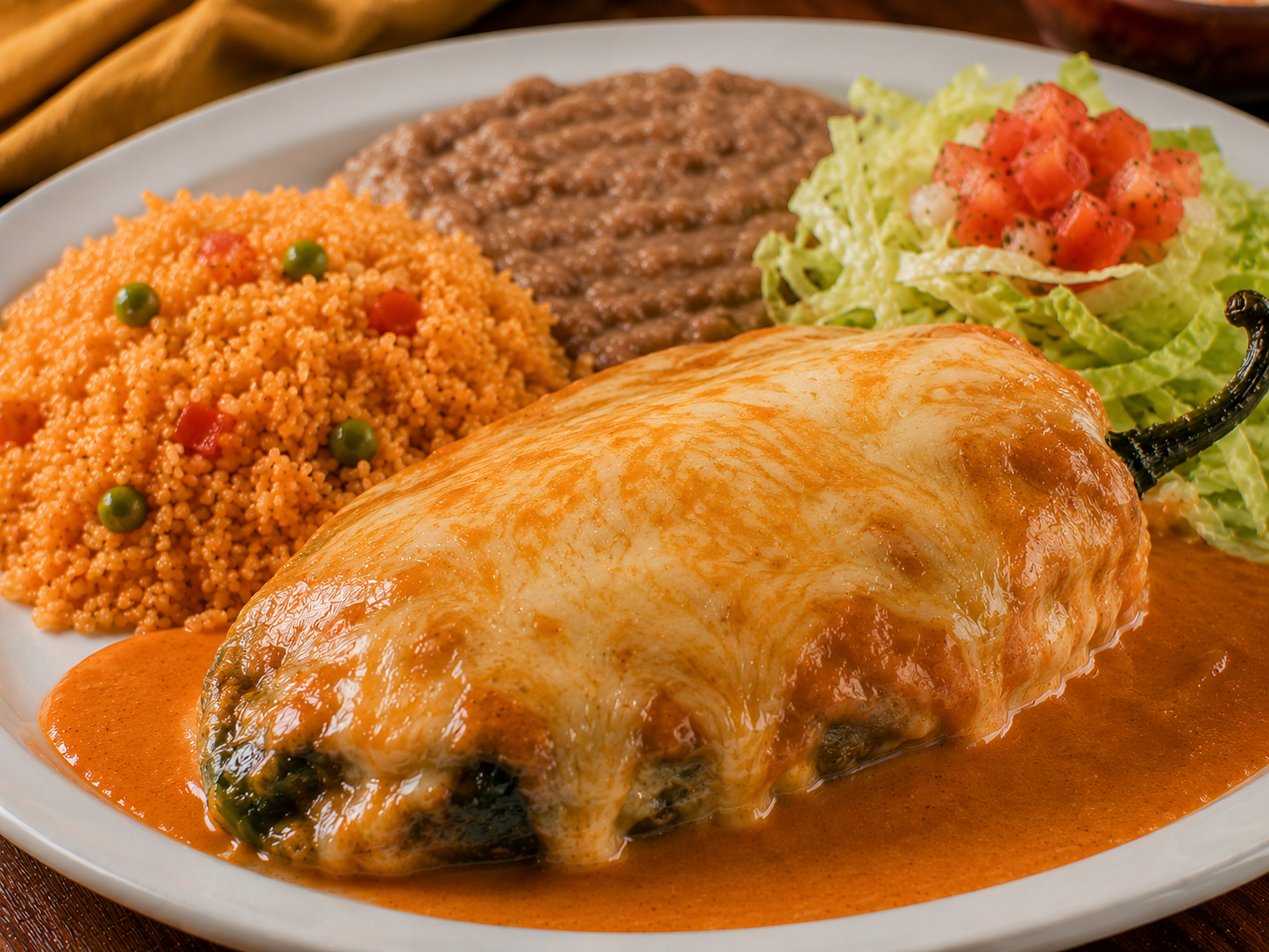 Chiles Rellenos plate served with guacamole, rice, beans, pico de gallo, and salad on a white plate