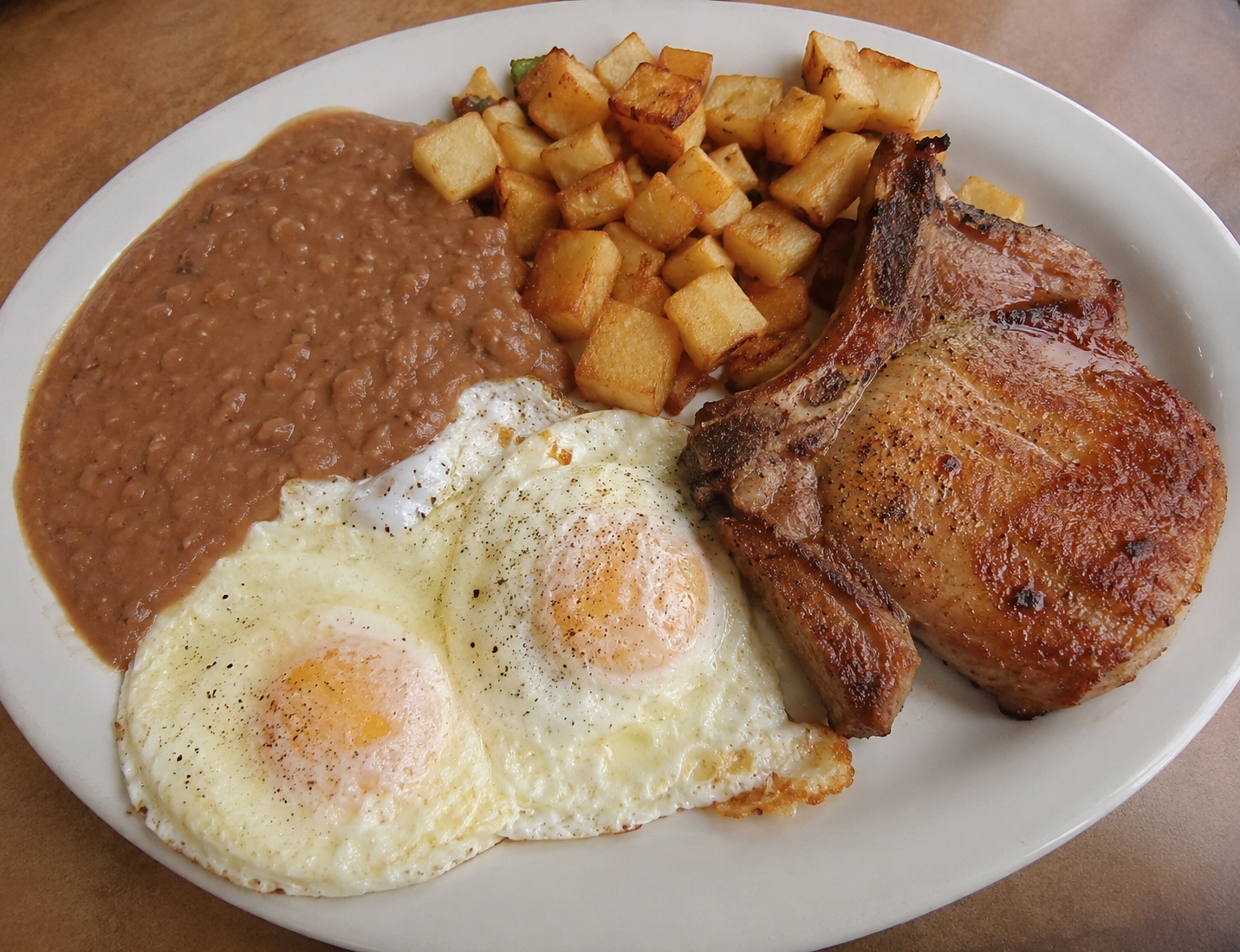Eggs with Pork Chops served on a white plate with a side of refried beans and potatoes