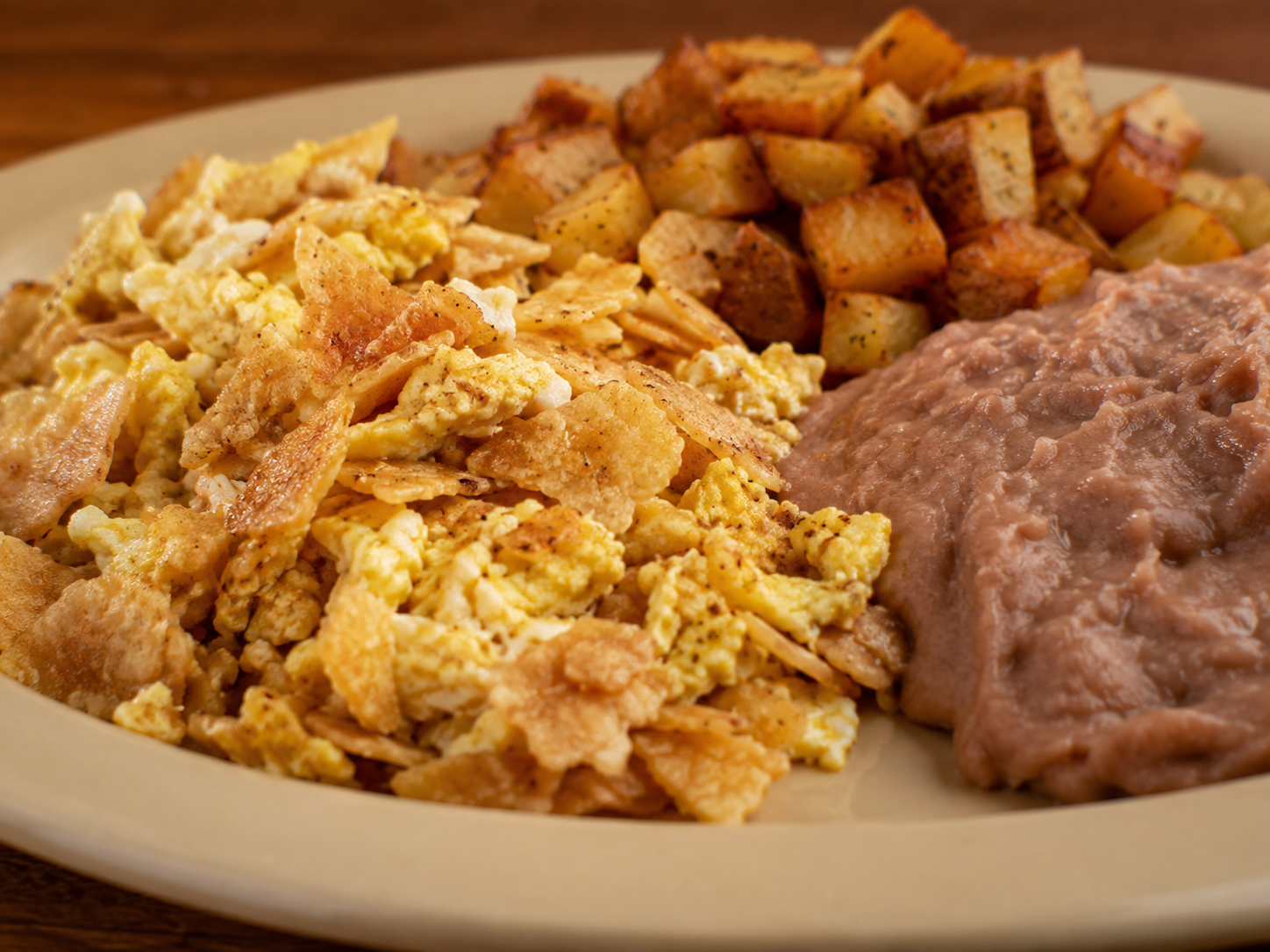Migas con Huevo with crispy tortilla strips, scrambled eggs, onions, tomatoes, and jalapeño peppers, served on a white plate with a side of refried beans and potatoes