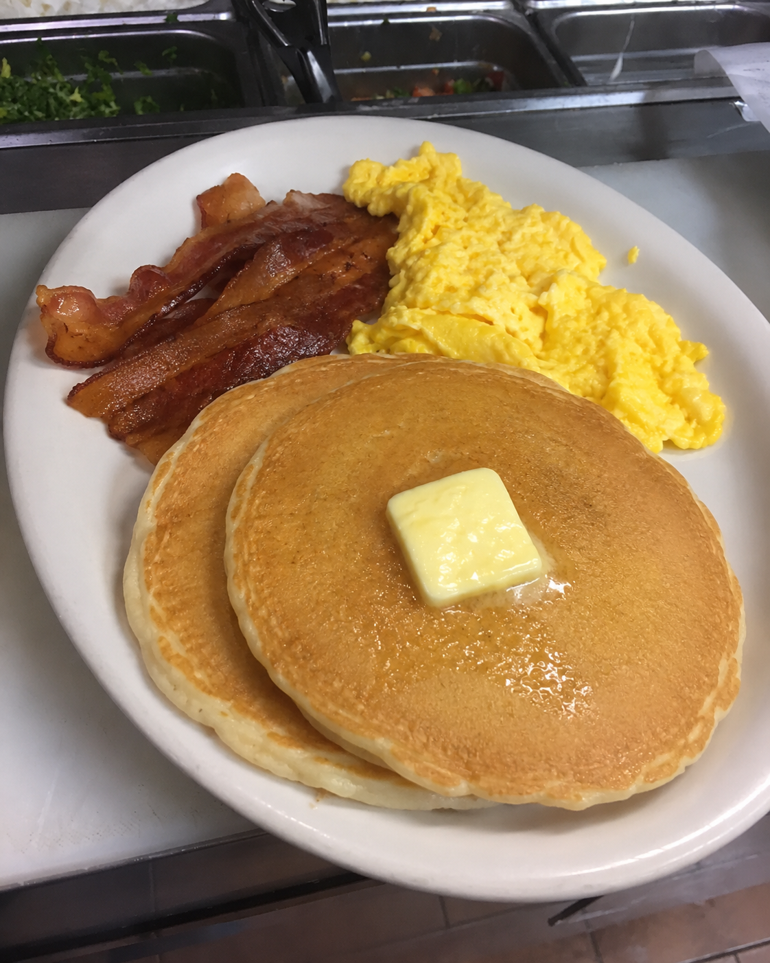 Stack of fluffy pancakes drizzled with syrup and topped with a pat of butter, served on a white plate
