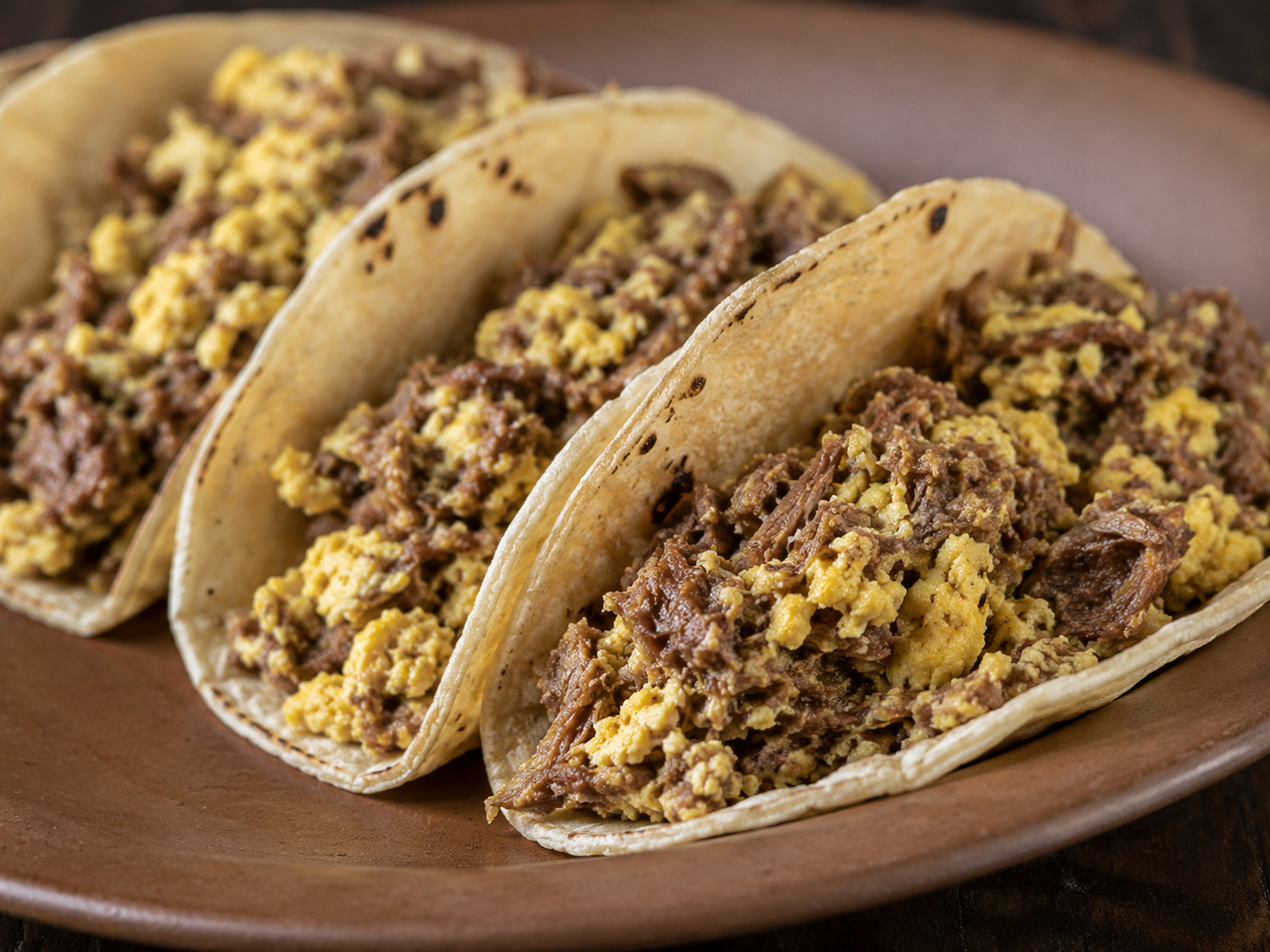 Taco Machacado served on a white plate with a side of refried beans and potatoes